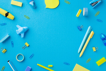 Back to school concept. Top view photo of yellow and blue stationery adhesive tape sharpeners stapler erasers binder clips corrector marker pens isolated blue background with empty space in the middle