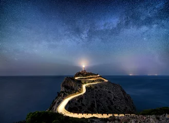 Poster Im Rahmen Night time image with milky way stars and illuminated road with light trails at the Far de Formentor lighthouse on Mallorca, Spain © Donald