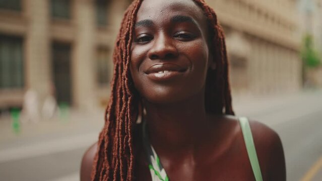 Close-up of beautiful woman with African braids raising her head and looking at the camera with smile on the building background. Close-up Slow Motion