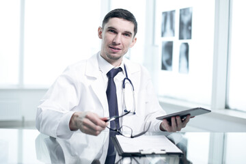 Doctor in his office at the clinic works sits at a glass table