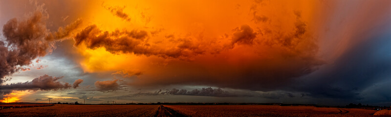 Panoramafoto einer abziehenden Gewitterwolke, die vom Licht der untergehenden Sonne orange...