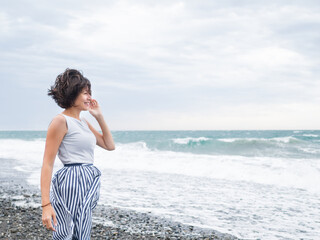 Happy woman greets stormy sea on pebble beach. Woman with hair ruffled with the wind. Wanderlust...
