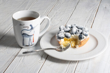 A cup of tea with the inscription don't worry and a bitten cake with blueberries