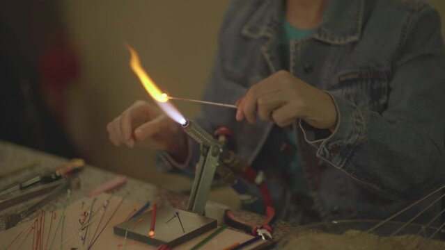 close-up video shot of woman making handmade glass beads with fire