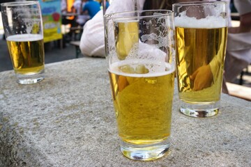 Drei gefüllte Biergläser auf Betonmauer vor Festplatz bei Sonne am Abend im Frühling 