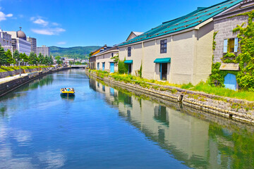 Fototapeta na wymiar 新緑の北海道小樽市、浅草橋街園から見る快晴の小樽運河の倉庫群と運河クルーズ船 