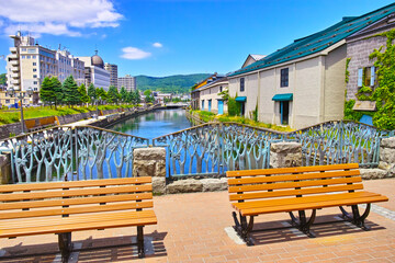 Fototapeta na wymiar 新緑の北海道小樽市、浅草橋街園から見る快晴の小樽運河の倉庫群とベンチの風景 