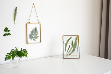 Composition of golden glass photo frames with green leaves on white table. Stylish home decor. Modern interior design.