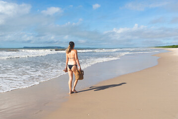 Woman in bikini walking on beach sand against blue sky.