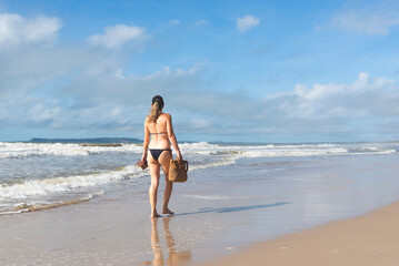 Woman in bikini walking on beach sand against blue sky.