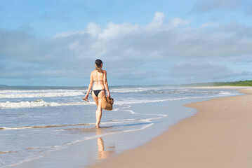 Woman in bikini walking on beach sand against blue sky.