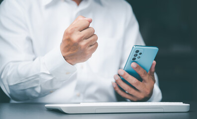 Young businessman clenching his fists showing joy in the success of the work through the mobile phone,