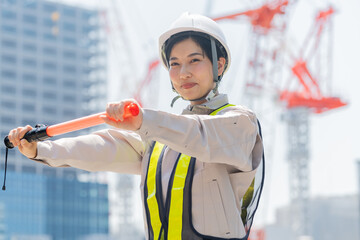 誘導棒を持ち笑顔でカメラを見る工事現場で働く女性