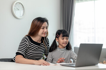 Asian little young girl kid learning online class at home with mother. Preschool child use laptop computer do homework, homeschool from school teacher by digital remote internet with support from mom.