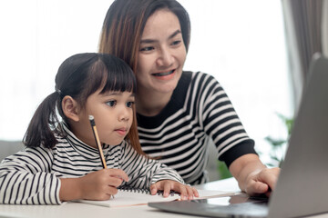 Asian little young girl kid learning online class at home with mother. Preschool child use laptop computer do homework, homeschool from school teacher by digital remote internet with support from mom.