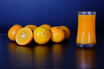 Close-up and vivid studio shot, a glass of orange juice, and a group of natural fresh oranges on...