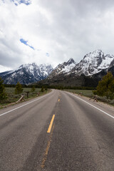 Fototapeta premium Scenic Road and Snowy Mountains in American Landscape. Spring Season. Grand Teton National Park. Wyoming, United States. Nature Background.
