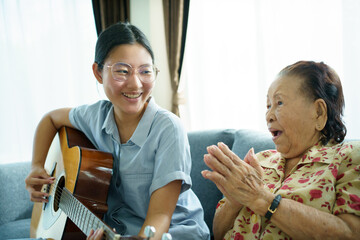 Asian elder woman playing an acoustic guitar and let her granddaughter taking a video on smartphone.
