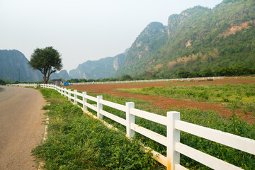 Fototapeta na wymiar White concrete fence around the agriculture farm or ranching near the complicated mountain with road and sunlight background at the Ban Rai ,Uthai Thani, Thailand.
