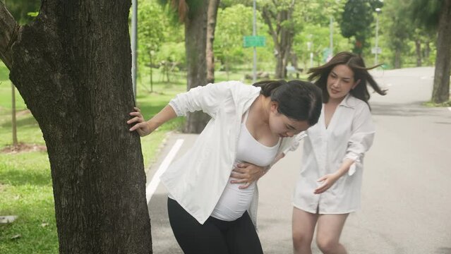 Young asian pregnant woman pain belly while people help and support in the park, maternity and help, pregnancy and medical, healthcare and sickness, lifestyles concept.