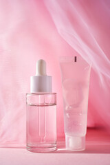 A transparent bottle of cosmetic gel and a bottle of serum on a pink background.