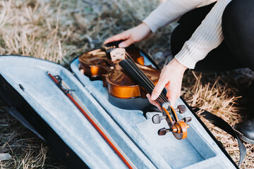 unrecognizable woman taking the violin out of its case in nature