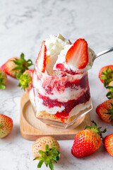 Strawberry mousse cake in a glass placed on a marble table. The distinctly layered strawberry mousse cake is beautifully decorated with sliced fresh strawberries.