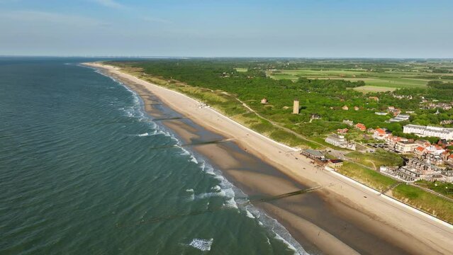 Aerial shot of changing tides outside a picturesque little coastal town in a green, rural area, on a beautiful summer day