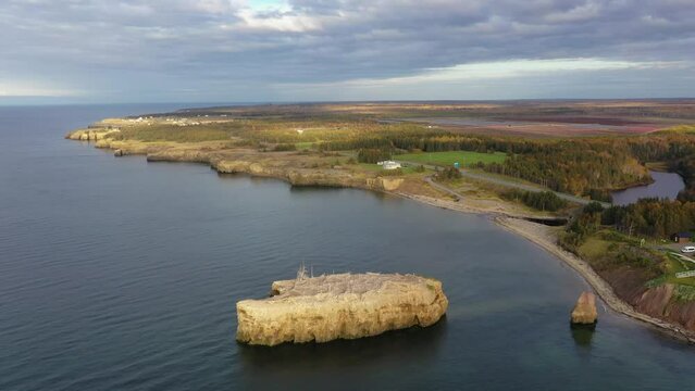 Slow motion drone footage on the scenic shoreline of Caraquet, New Brunswick, Canada. Scattered clouds and blue sky over landscape in fall colors.