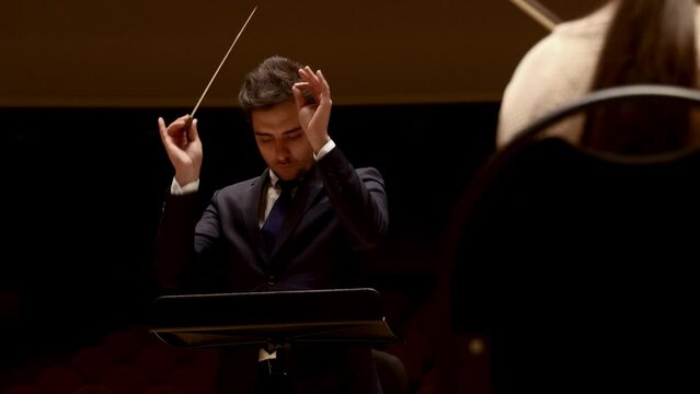 Conductor of symphony orchestra with performers in background in concert hall. High quality 4k footage
