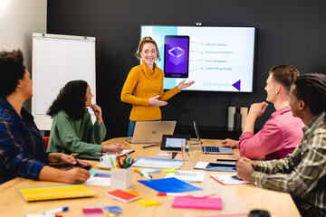Smiling caucasian businesswoman discussing ideas with app developers in meeting at office