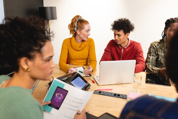 Female caucasian app developer discussing with biracial colleague over laptop in meeting at office