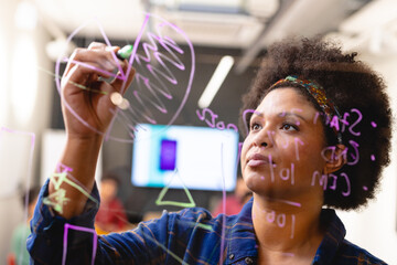 Young african american female app developer drawing chart on glass in board room