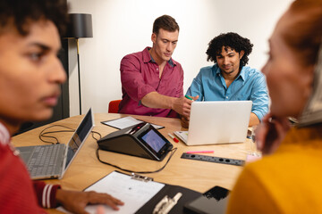 Male caucasian app developer discussing with biracial colleague over laptop in meeting at office