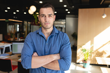 Portrait of confident young caucasian creative businessman with arms crossed in office