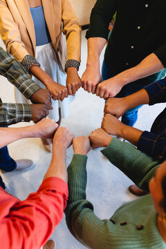 Multiracial male and female colleagues huddling with clenched fists in office
