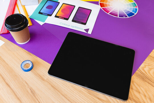 High angle view of digital tablet with disposable coffee cup and color swatch at desk, copy space