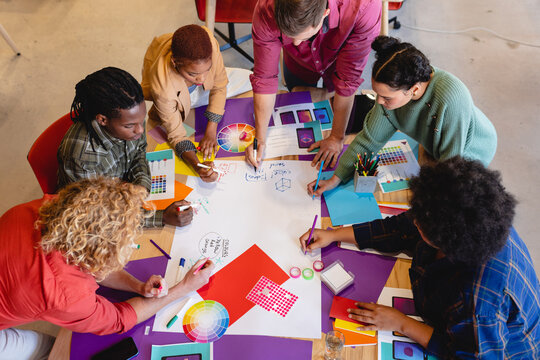 High angle view of multiracial design professionals writing ideas on paper during meeting in office