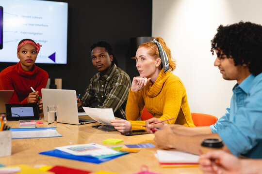 Serious female caucasian app developer with colleagues in board room at office