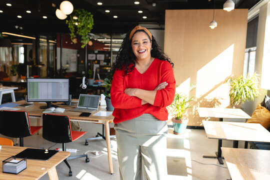 Portrait of happy biracial creative businesswoman with arms crossed in office