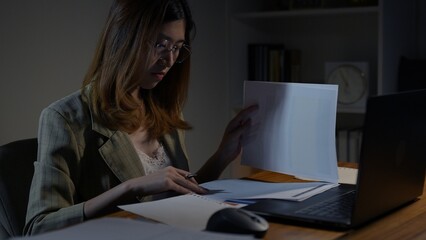 Asian businesswoman or freelancer working hard at the night looking the laptop digital tablet and document in workplace at late overtime deadline, Stressed busy and exhausted of work at home.