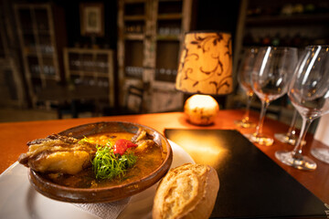 restaurant table with Bolivian fricassee plate with a closed menu, glasses, a small lamp with warm light and a cabinet with bottles and glasses in the background
