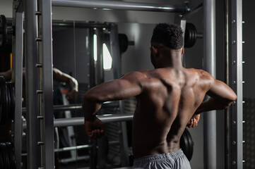 Handsome afro american man posing showing back muscles in gym. 