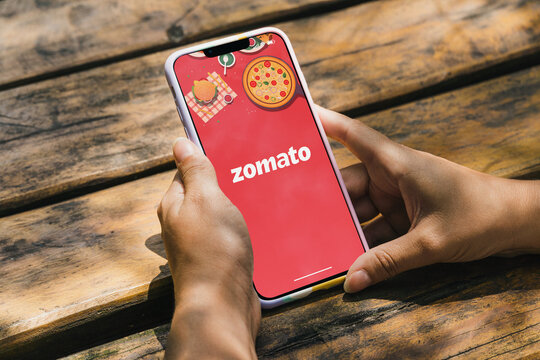 Girl in the park holding a smartphone with Zomato food delivery app on the screen. Rustic wooden table. Rio de Janeiro, RJ, Brazil. July 2022