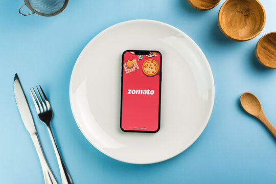 Zomato food delivery app on smartphone screen on top of white plate. Beside cutlery and utensils. Waiting for delivery to eat the food. Rio de Janeiro, RJ, Brazil. July 2022.