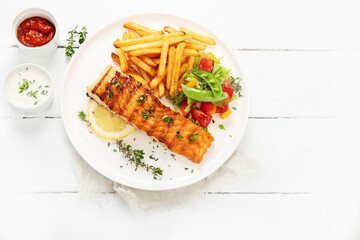 Salmon steak with vegetables and fries on light background.