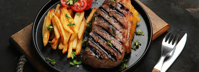 Striploin beef steak with french fries on dark background.