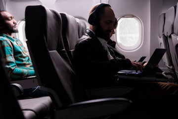 Multiethnic group of travellers sitting in airplane seats to fly abroad, travelling to business trip or holiday vacation with international airline. Diverse people flying in economy class.