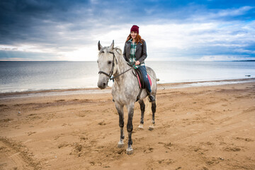 Fototapeta na wymiar dressing jeans, jacket and spring hat female horse jokey rides a dappled hackney along seashore