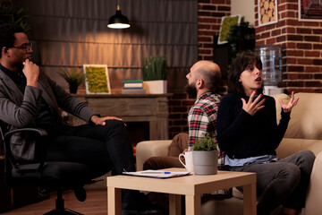 Husband and wife fighting at couple therapy session with counselor, sitting back toback to talk about problems. Therapist giving advice, trying to solve relationship issues between partners.